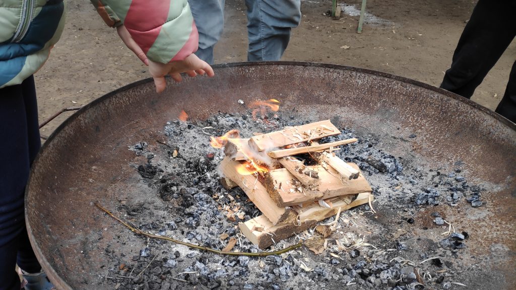 gestalpeltes brennendes Holz in einer Feuerschale ein Kind wärmt sich die Hände
